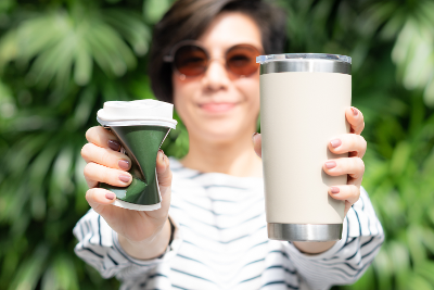 Woman with scrunched up non-recyclable coffee cup and a reusable cup